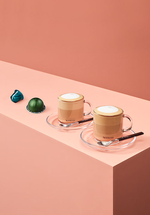 Two coffee cups on the table with both original and vertuo capsules 